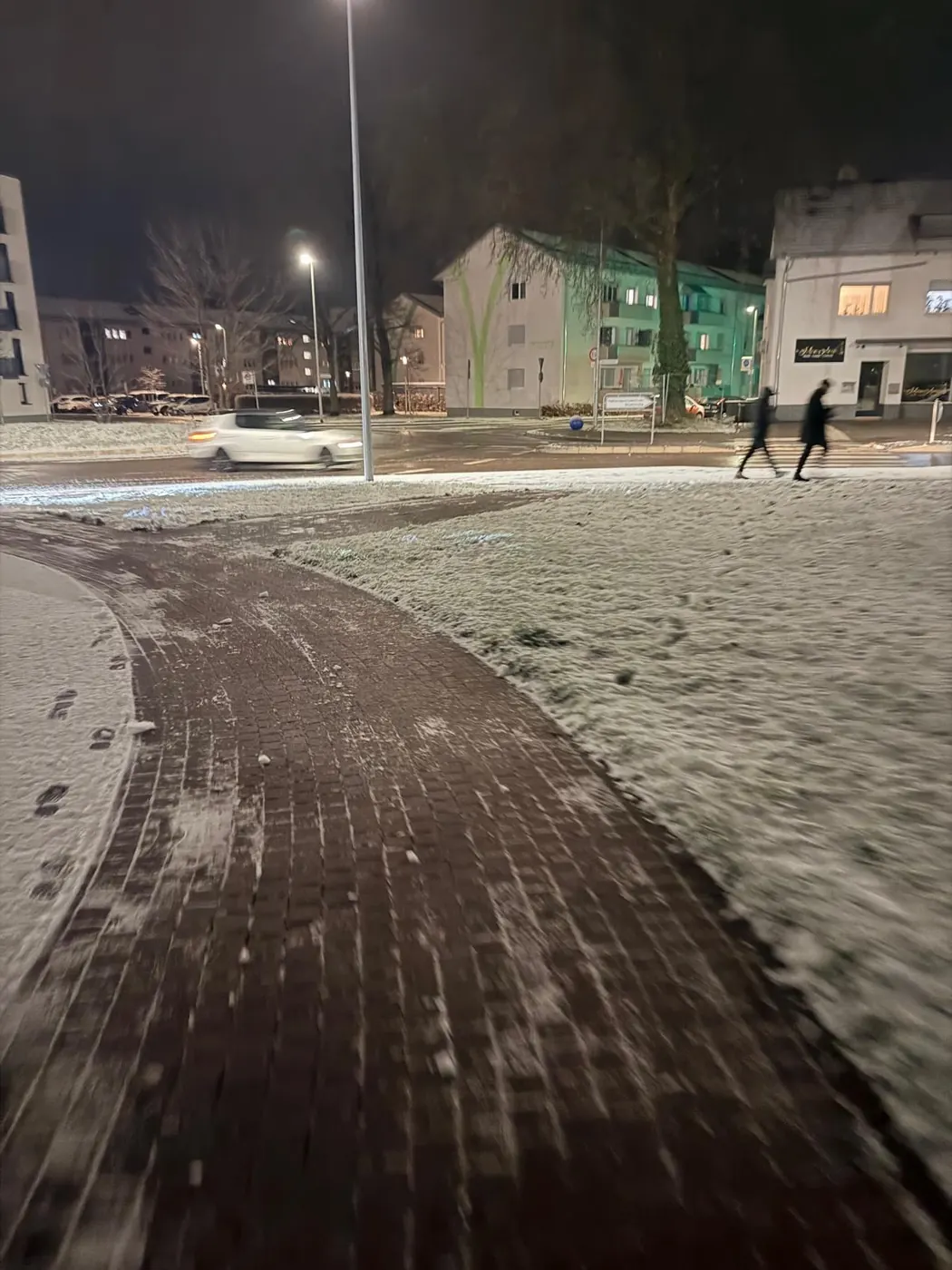 Geräumter und gestreuter Gehweg bei Nacht neben verschneiter Grünfläche – Winterdienst in Lahr durch Schmidt Hausmeisterservice